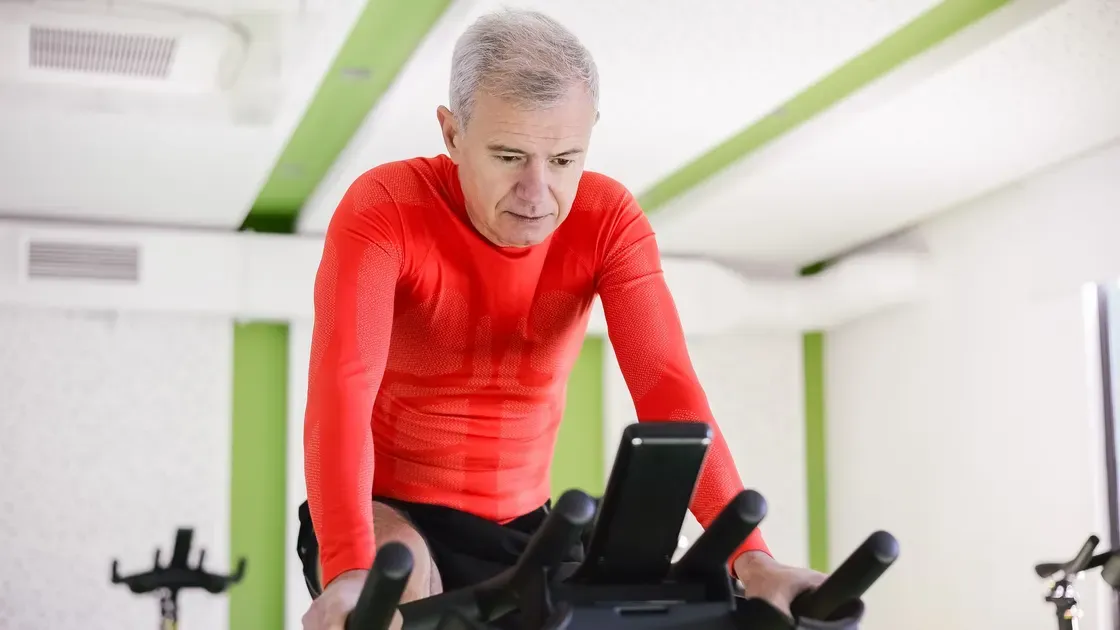Gråhårig man i röd tröja tittar på displayen på en motionscykel