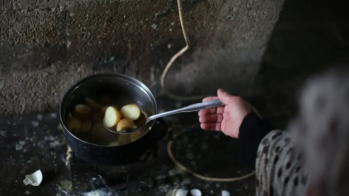 En hand lyfter upp skalad potatis ur en kastrull med vatten med en slev
