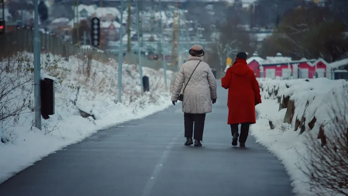 Två personer promenerar på en snöröjd gångväg med snövallar på båda sidor en vinterdag