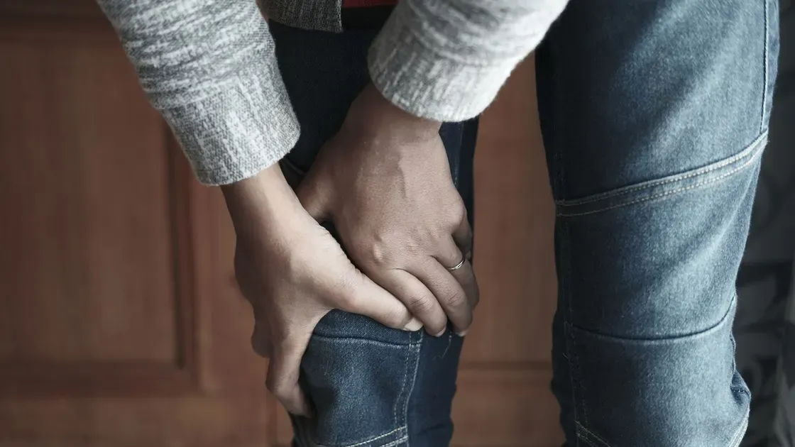 Person i jeans står böjd och håller om det värkande knät med båda händerna