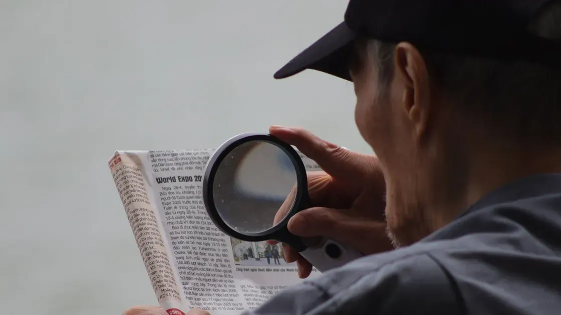 Man med keps läser en tidning utomhus genom ett runt handhållet förstoringsglas