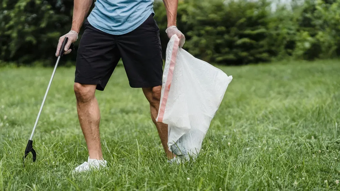 Person med griptång och påse plockar skräp på en gräsmatta
