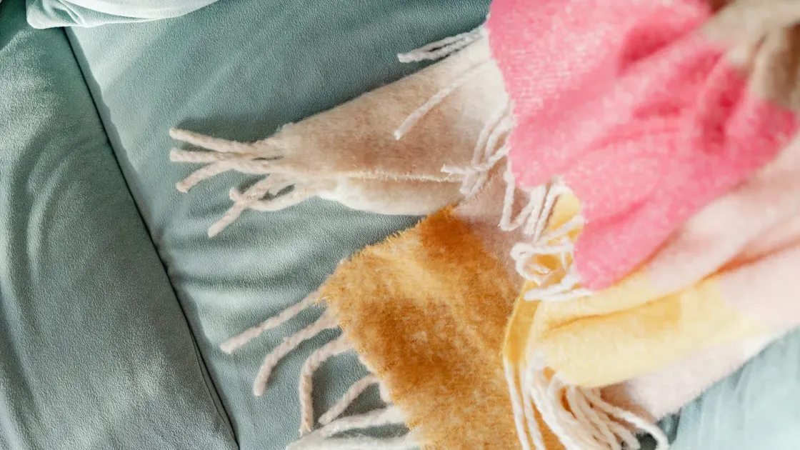 Närbild på fransarna och de rosa och gula fälten i en pläd som ligger på en soffa