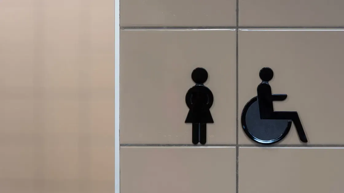 Svarta toalettskyltar för dam och rullstol på en kaklad vägg