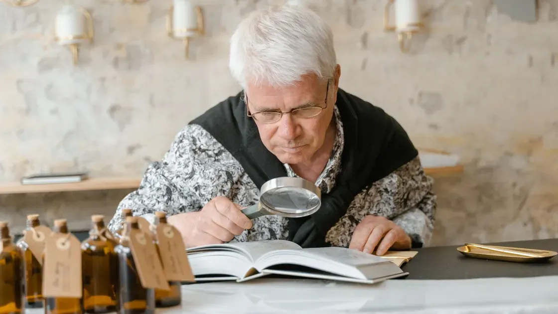 Äldre man håller ett handhållet förstoringsglas över en uppslagen bok och lutar sig nära sidan