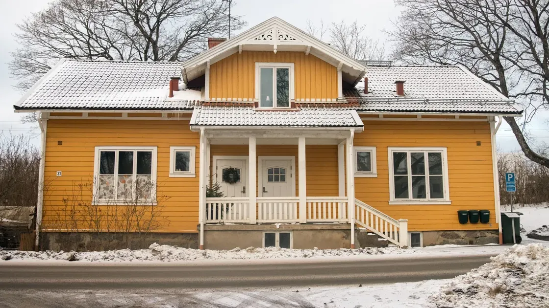 Äldre par i den öppna dörren till ett hus med slitna putsade väggar