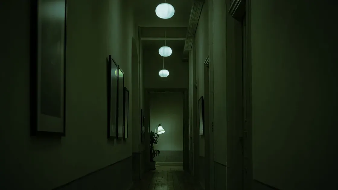 Mörk hall på natten med svagt tända taklampor och en bordslampa längst bort