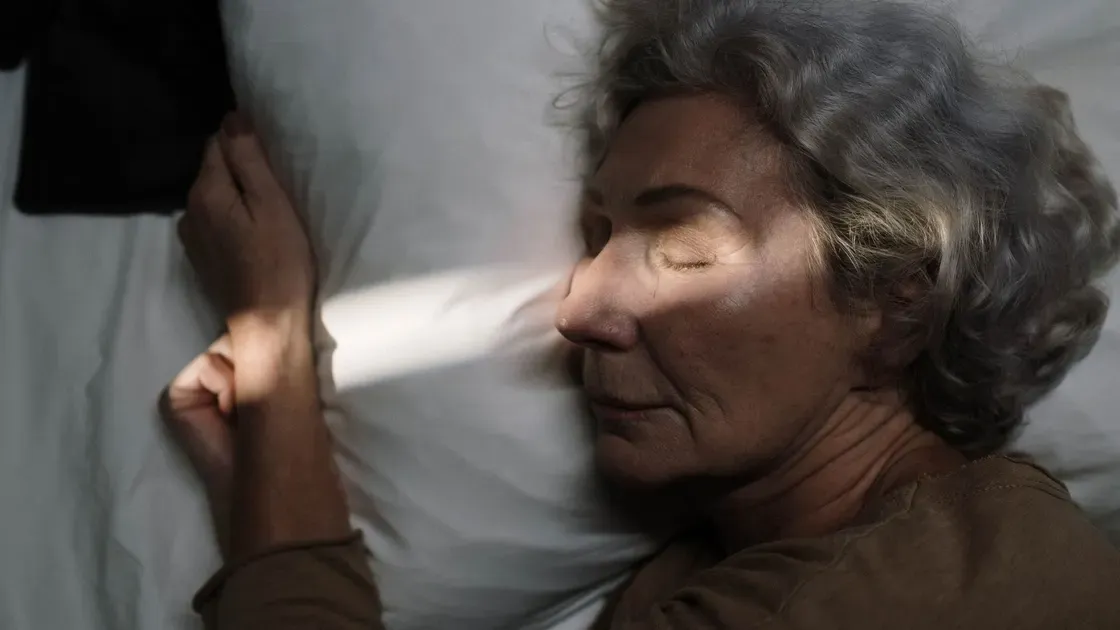 Äldre kvinna sover på sidan med kinden mot en ljus kudde