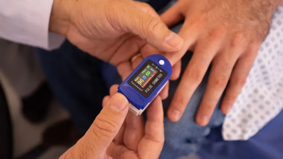 En blå pulsoximeter sätts på ett finger och skärmen visar 96 procent syremättnad och puls 69