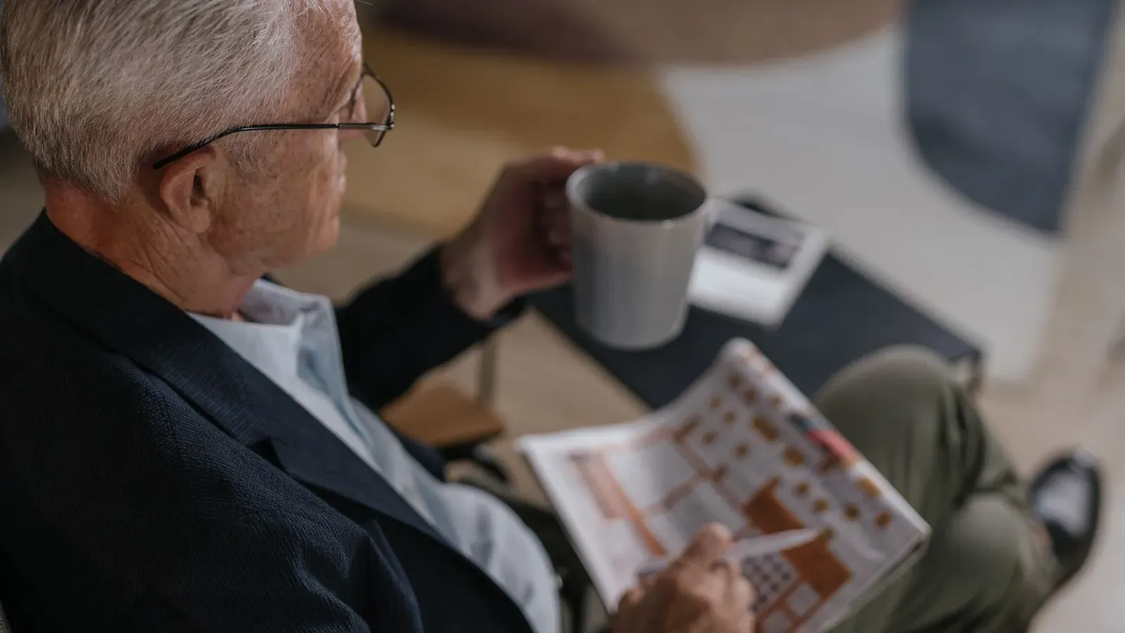 Äldre man med glasögon läser en tidning med en kaffekopp bredvid sig